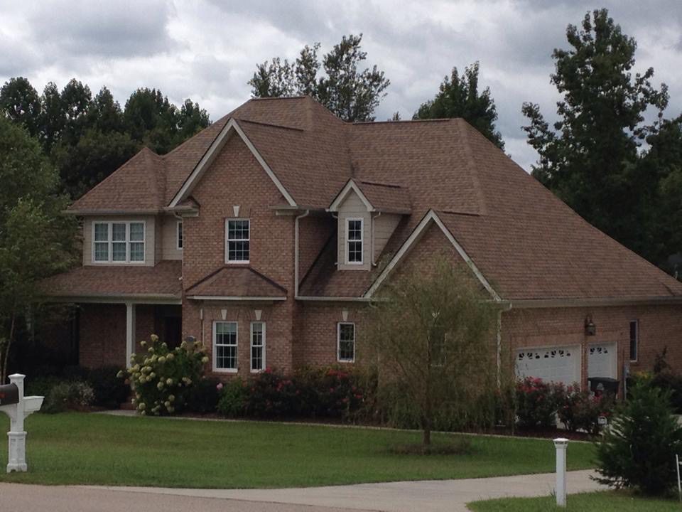 A large suburban house with a brown roof and well-maintained lawn.