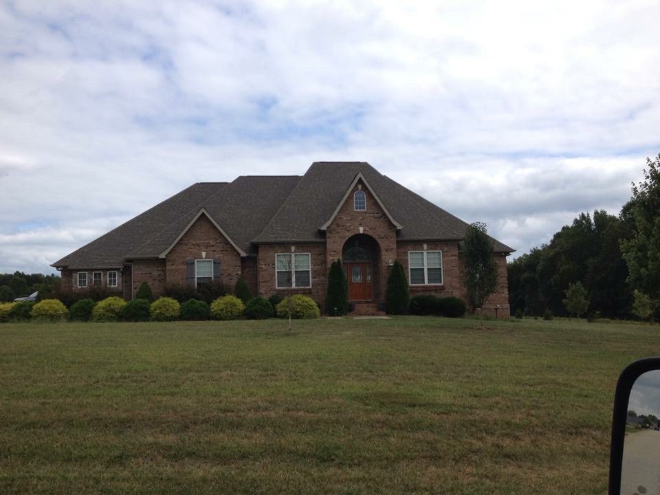 Large brick house with a spacious front lawn under a cloudy sky.